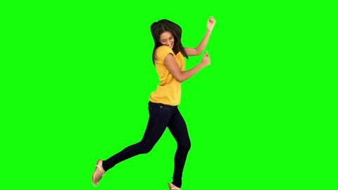 Cheerful woman jumping with legs and arms raised on green screen in slow motion