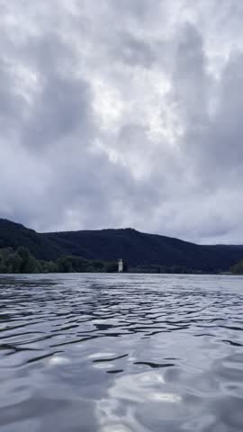 Timelapse of rippling river water under dramatic cloudy sky with dark hills on horizon, moody nature landscape, changing light and moving surface texture.