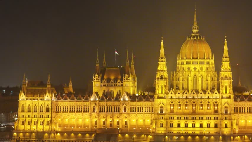 Aerial close-up tracking right of the stunning illuminated Neo-Gothic facade and central dome of the Hungarian Parliament Building in Budapest at night