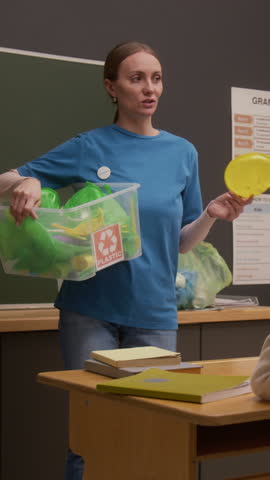 Vertical shot of young woman as eco volunteer holding sorting bin and explaining plastic recycling while giving lecture in school