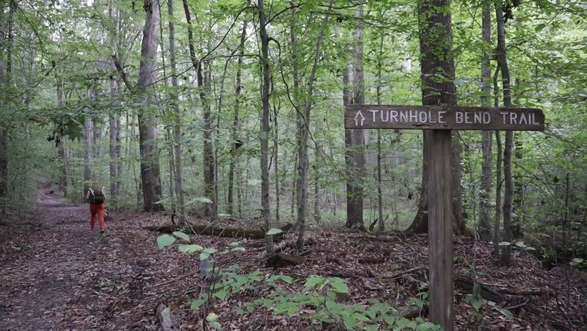 A backpacker hikes down a Turnhole Bend Trail at Mammoth Cave National Park through a Fall forest, past the wooden trailhead.