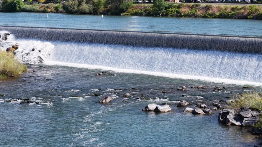 Aerial footage of a cascading weir on the Snake River with birds resting on rocks below and surrounding trees and farmland near Idaho Falls