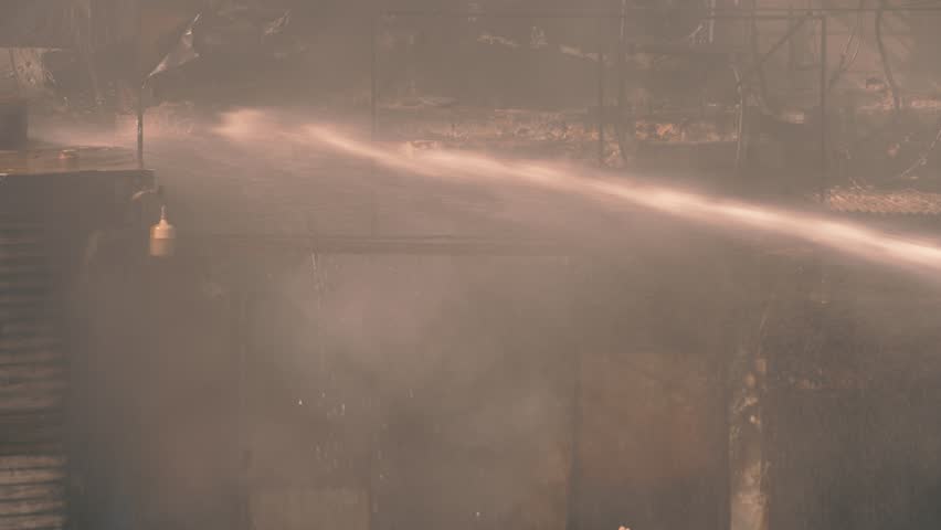 Firefighter spraying water jet to extinguish a fire creating smoke and destruction