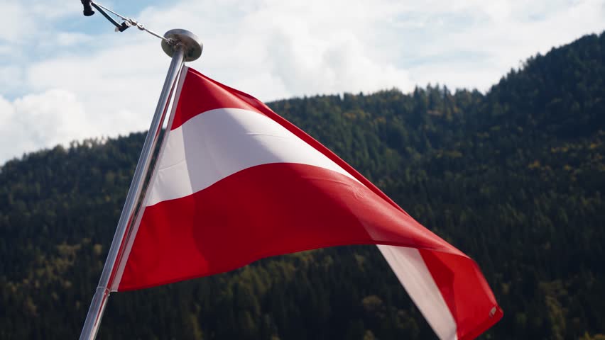 Austrian flag waving in the wind with Alpine mountain forest scenery