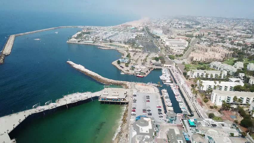 Aerial view of Redondo Beach, California, showing harbor, marina, breakwater, coastline, beachfront neighborhoods, roads and Pacific Ocean under clear daylight. Wide shot.