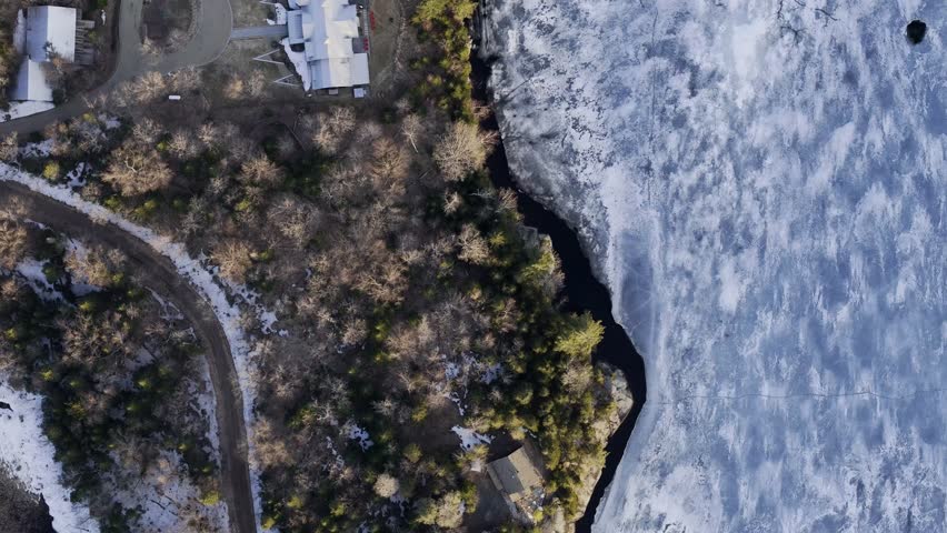 Aerial view of frozen lake in Quebec with forest and mountains winding road along under blue sky. g.