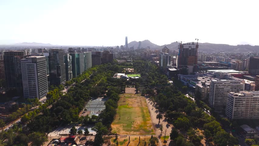 Panoramic aerial sweep over Parque Araucano in Las Condes, highlighting the expansive green spaces, recreational areas, and surrounding modern skyline of Santiago's financial district.