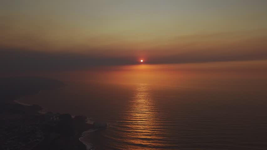 Breathtaking aerial view of the sun setting over the endless Pacific Ocean, creating a dramatic path of golden light reflections on the water.