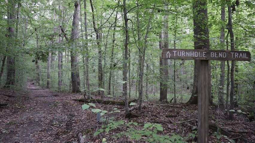 A backpacker hikes along an Autumn trail. She stops and gives a thumbs up to the camera. Filmed at Turnhole Bend Trail at Mammoth Cave National Park.