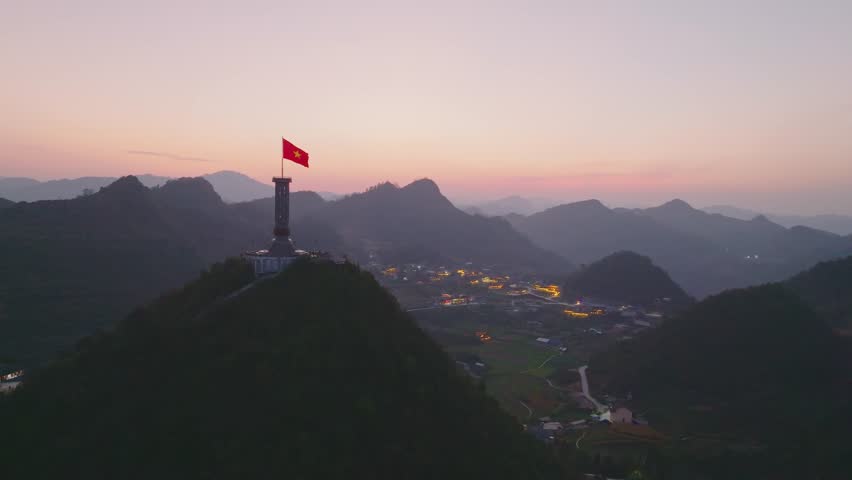 Wide twilight panorama of Lung Cu Flag Tower overlooking illuminated valley and layered mountains.