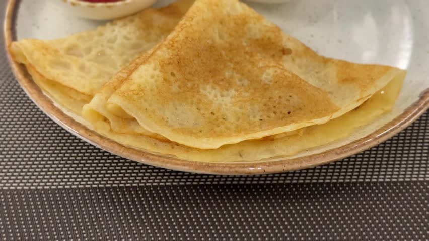 Thin crepes on a ceramic plate with accompanying raspberry sauce in background video