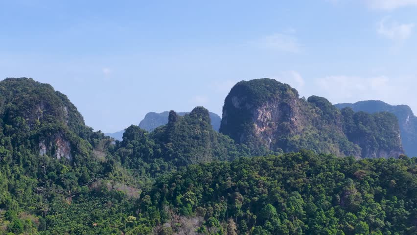 Wide shot of lush tropical forest and limestone karst mountains under a clear blue sky