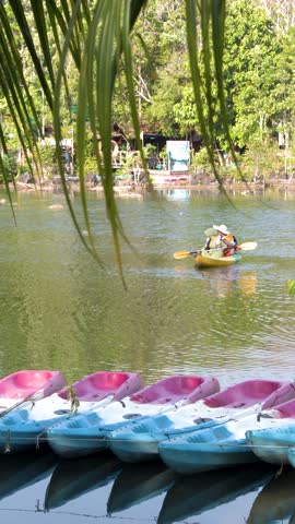 Two people paddle a yellow kayak across a calm tropical lake past docked colorful boats