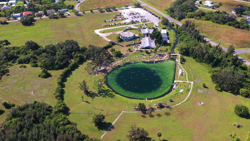 Overhead view of famous Florida Warm Mineral Springs in North Port, showing people swimming in circular lagoon, vibrant blue water and natural geological formation used for therapy.