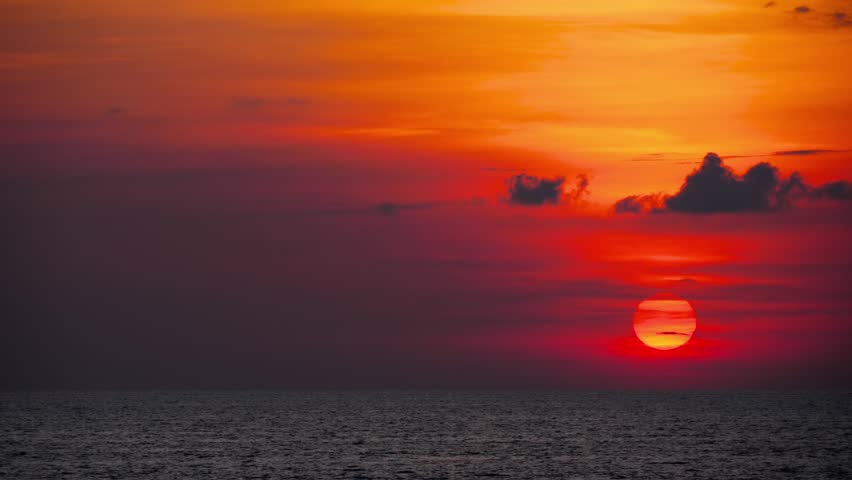Dramatic red sunset over the ocean, with glowing skies and calm waters, creating a serene and picturesque evening landscape.