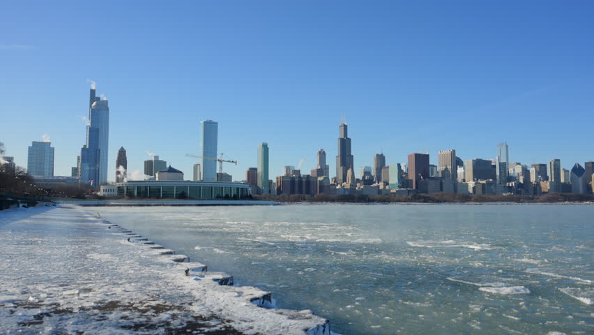 Chicago skyline with frozen Lake Michigan and ice formations, winter urban waterfront landscape under clear blue sky.