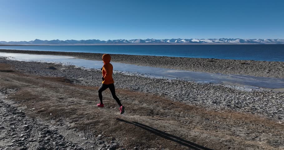 Woman runner running at the winter high altitude lakeside, Tibet, slow motion