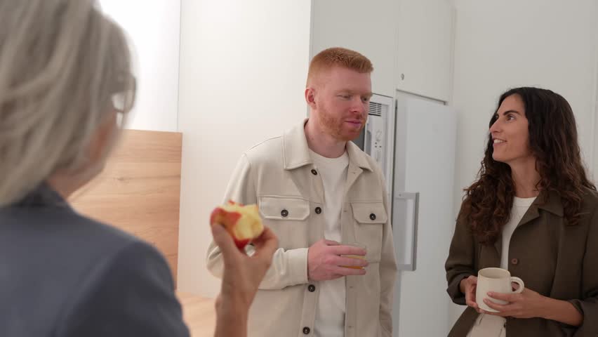 Three diverse colleagues interacting in a modern office kitchen. Young coworkers and a senior manager enjoying a casual conversation during a break