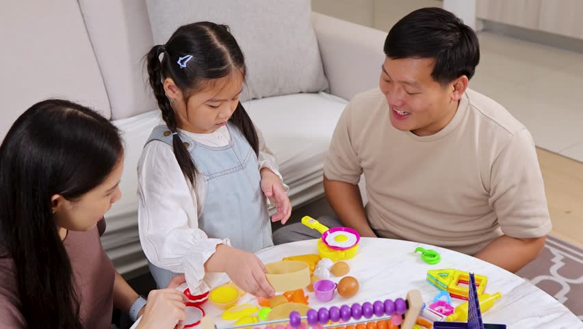 Asian family with young girl playing with educational toys at home in bright living room.