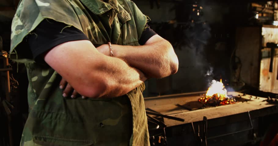 Camera pulling back, blacksmith holding crossed arms in forge, code overlays visualizing tech data. Industrial, workshop, metalworking, furnace, sparks, smoke, binary