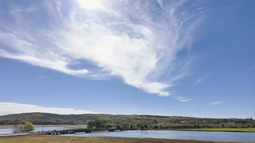 Slow motion footage scenic view of the Annapolis Royal tidal river crossing in Nova Scotia Canada featuring a historic steel bridge calm waters forested hills and dramatic cloud formations 