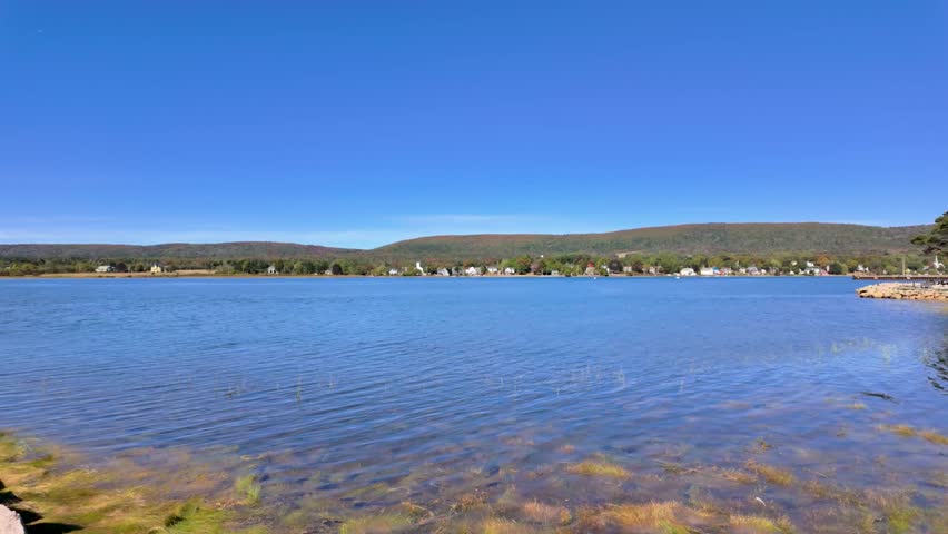 Slow motion footage view across the calm waters of Annapolis Basin in Annapolis Royal Nova Scotia Canada with distant shoreline homes rolling hills and clear blue skies creating a peaceful maritime 