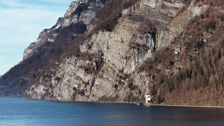 Steep limestone cliffs of Churfirsten rising above calm Walensee waters near Walenstadt, Switzerland.