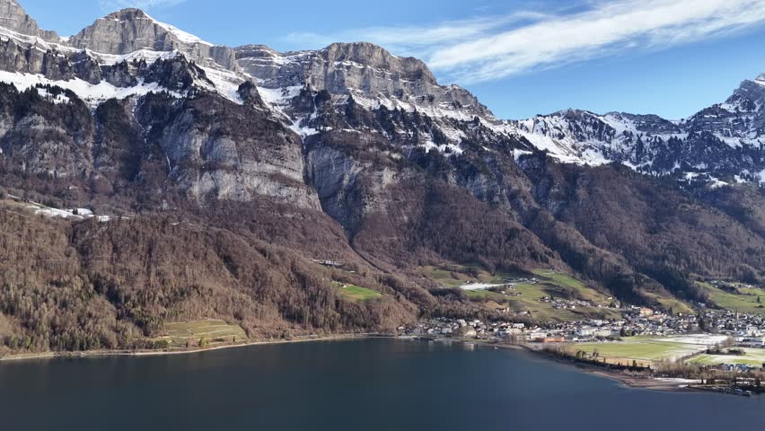 Aerial of the massive Churfirsten range in Switzerland. Majestic snowy peaks tower over the frosty valley floor, leading towards the town of Walenstadt.