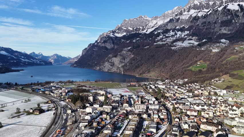 View of Walenstadt, Switzerland, at the eastern end of Lake Walensee. Snowy peaks of the Churfirsten tower over the winter valley and the calm, deep-blue waters.