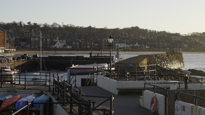 A peaceful scene of North Berwick Harbour at sunset, featuring stone walls, kayaks, and the coastal town skyline. Ideal for travel and Scottish tourism content.