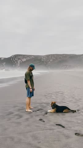 Man and Dog Playing on Beach with Ocean and Cliffs.

Man running and playing with his dog on the beach with ocean waves and cliffs.