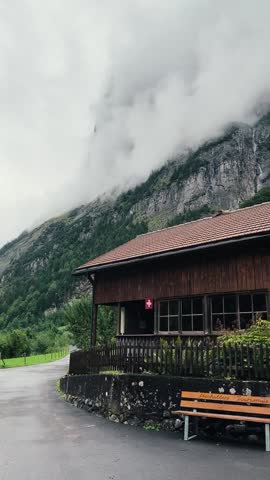Traditional Swiss Chalet with Mountains and Clouds.

Authentic Swiss wooden house surrounded by green hills, mountains and low clouds, peaceful alpine scenery.