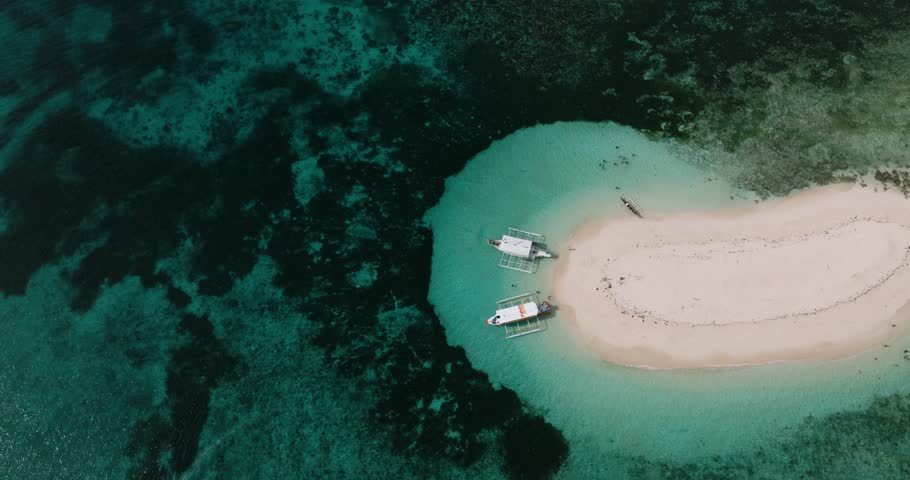 Boats anchored by a sandbar island in turquoise shallow sea water. Naked Island. Siargao, Philippines.