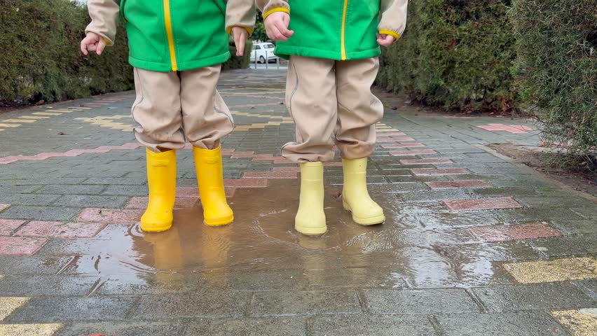 Kids standing in puddle after rain, puddle surface ripples, puddle reflections and fun moment showing simple outdoor joy and seasonal childhood experience. Rainy day joy and childhood outdoor fun.