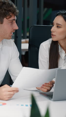 Two business colleagues talking research papers analyzing documents discussion work result in office businesswoman with businessman talk working discuss paperwork using laptop communicate together