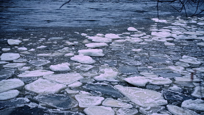 Layered ice chunks float and separate across rippling water as winter conditions recede on lakeshore, winter to spring transition