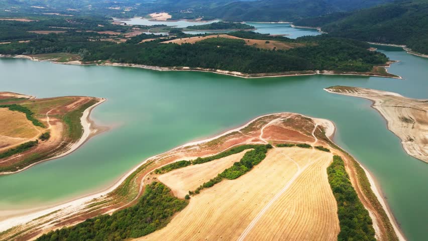 High drone push angled downward revealing Yovkovtsi Reservoir’s bluish green waters, winding shape, lush greenery, and surrounding hills.
