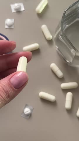 Overhead view of woman holding white capsule above pills 
