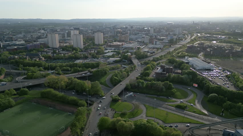 A highangle aerial view showcasing heavy traffic flow on urban motorways with the Glasgow city skyline and residential highrise buildings in the background.