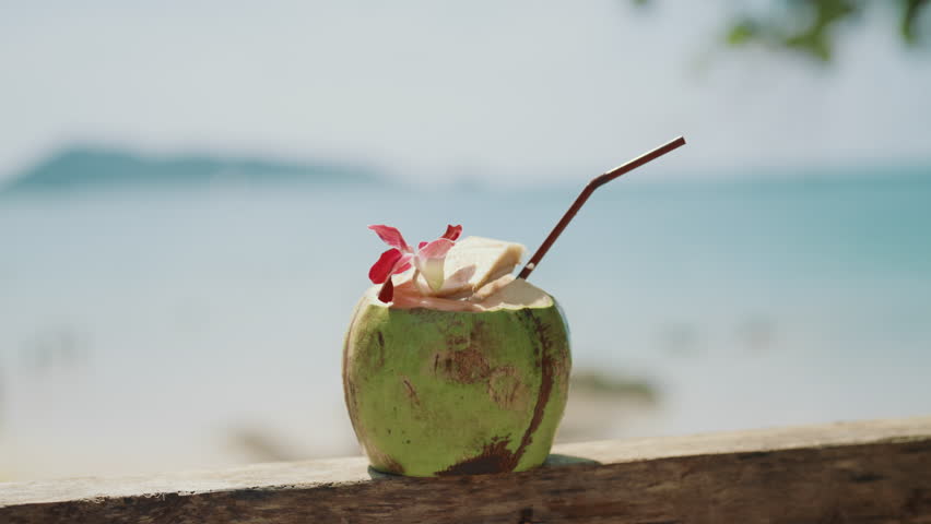 Coconut cocktail in beach bar, delicious refreshing soft drink, closeup view. Relaxation on ocean coast and enjoying fresh coconut milk, quenching thirst in hot summer day, vacation in islands