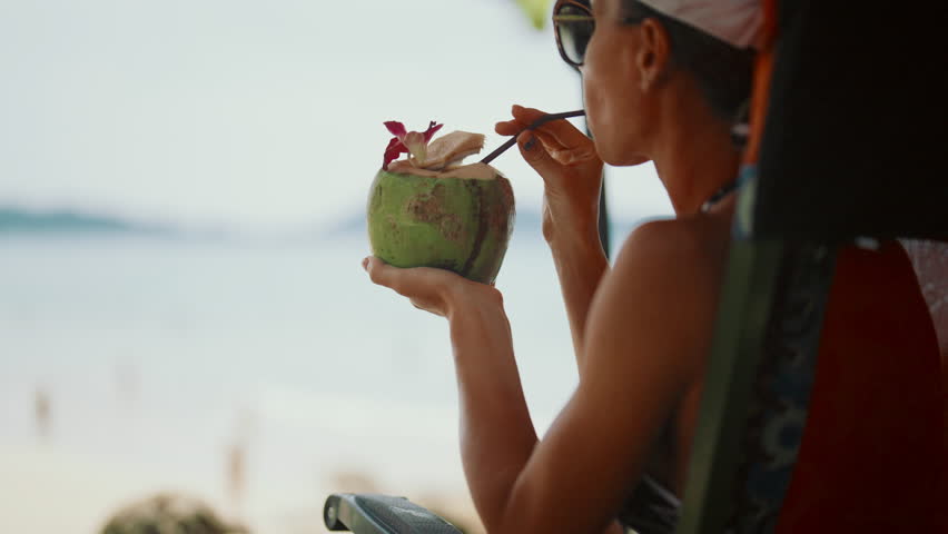 Summer vacation in tropical resort island, happy woman drinking coconut cocktail . Carefree female vacationer enjoying life and sipping fresh cold soft drink from coconut, trip to ocean in summer