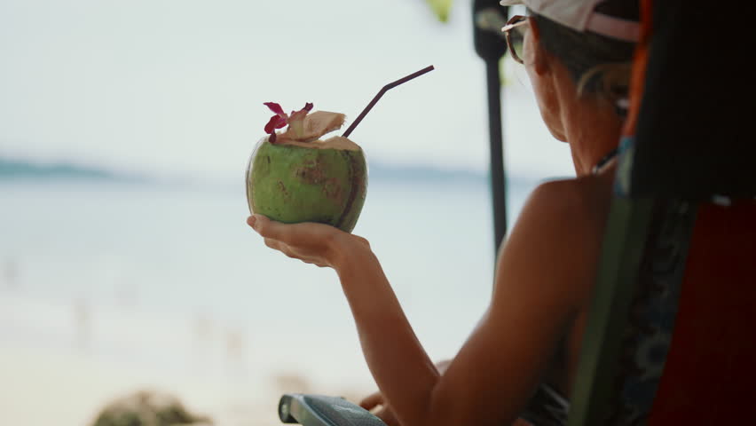 Summer vacation in tropical resort island, happy woman drinking coconut cocktail . Carefree female vacationer enjoying life and sipping fresh cold soft drink from coconut, trip to ocean in summer