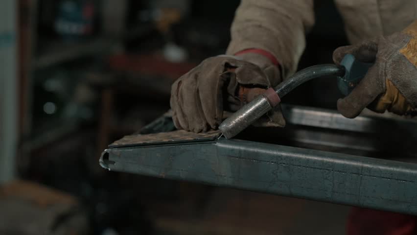 A close-up of a worker welding metal, with bright sparks flying as the torch fuses steel on an industrial workbench. Slow motion.