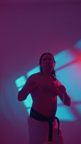 Male High Kick. Male Martial Artist Executing Energetic High Kick In Studio Environment. Caucasian Male Athlete Delivering Vigorous High Kick In Neonlit Studio Scene With Shadow Effects