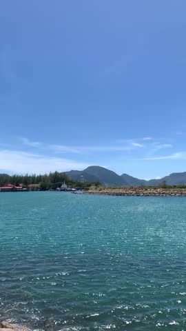 Coastal landscape with calm blue sea, mountains, and shoreline under clear sky