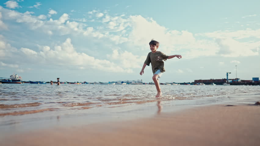 Child boy walking along ocean shore on yellow sand beach in summer. Vacation.