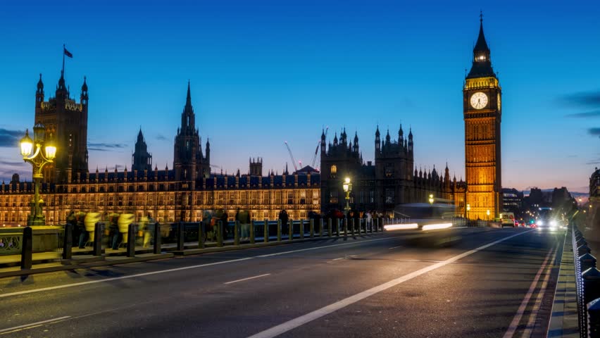Time lapse view of the illuminated Big Ben tower and Westminster Palace in London, England, during evening with blurred street traffic and light trails
