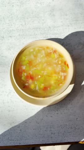 4K Vertical Top down shot of a vegetable soup in a bowl. Female hand drink soup with help of spoon. Soup on a table. Woman eating fresh homemade vegetable soup at table, top view. Healthy eating concept.