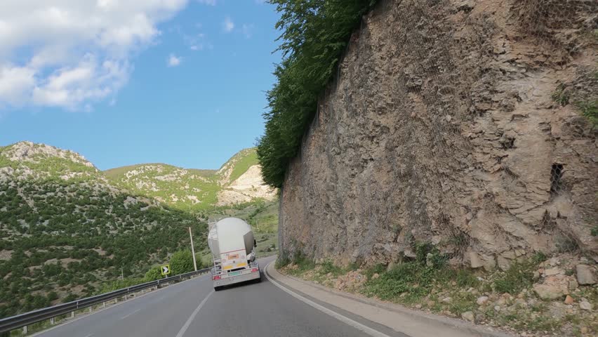 Tank cistern truck driving on a scenic road through mountain landscapes under a blue sky