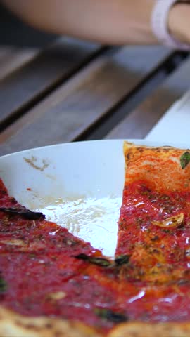 Close up view of a person taking a slice of delicious marinara pizza from a plate on a wooden table, enjoying an italian meal at a restaurant with friends during lunch or dinner